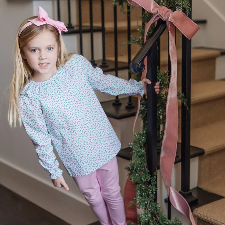 Young girl in a light blue floral top and pink pants standing on a staircase with decorative ribbons.