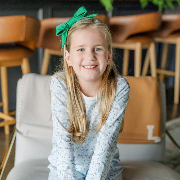 Young girl with a green bow in her hair sitting on a chair indoors.