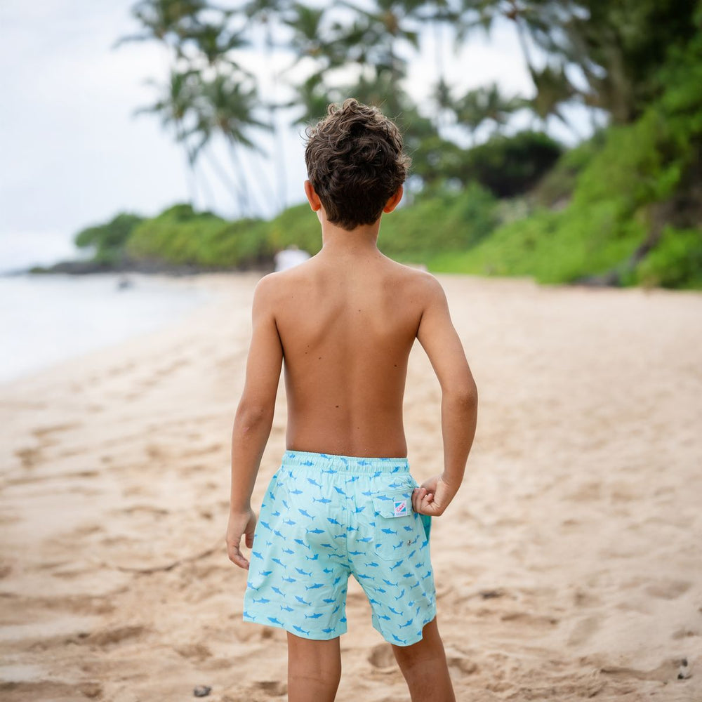 Child wearing light blue swim shorts with a pattern on a beach