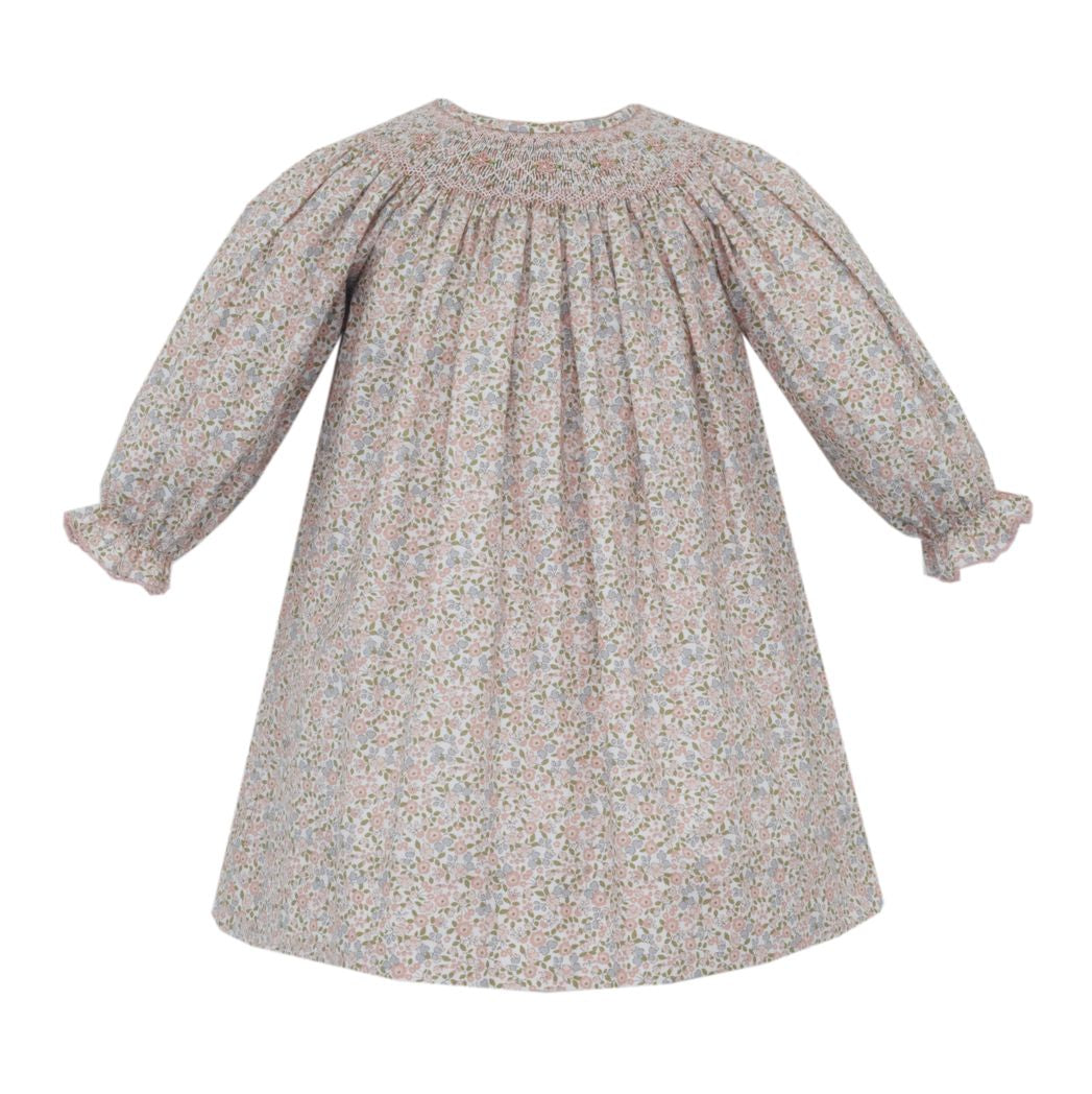 A long-sleeve baby dress with a delicate multicolor floral print on a light beige background, featuring a smocked bodice and ruffled cuffs, shown against a plain white background.