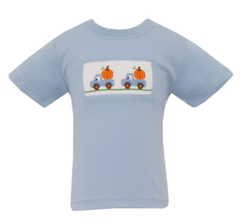 A light blue short-sleeve baby t-shirt with a rectangular patch on the chest depicting two blue pickup trucks carrying orange pumpkins. A smaller inset image on the right shows a close-up of the embroidered patch.
