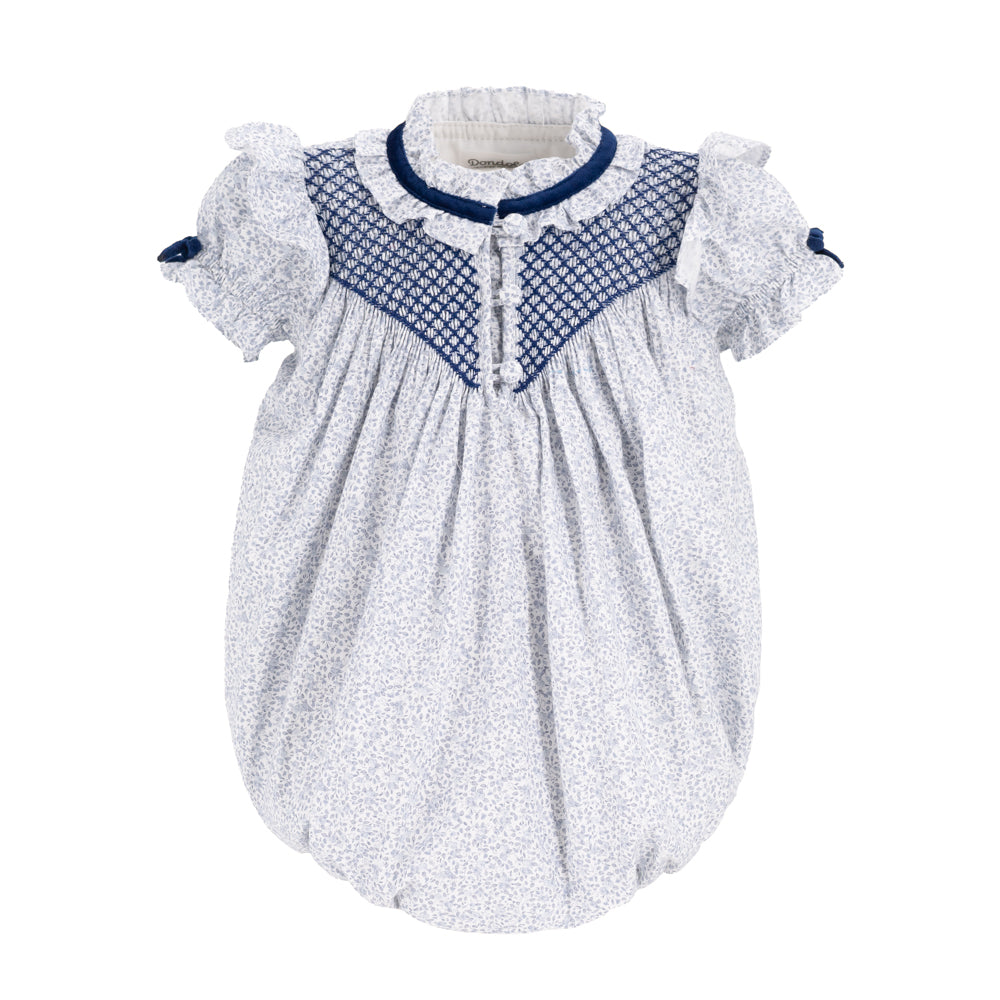 A baby smocked dress with a white and blue micro-patterned body, a navy blue smocked yoke, and ruffled short sleeves with navy bows, shown on a plain white background.