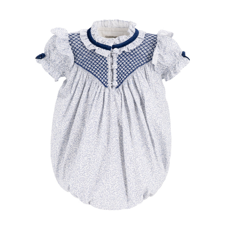 A baby smocked dress with a white and blue micro-patterned body, a navy blue smocked yoke, and ruffled short sleeves with navy bows, shown on a plain white background.