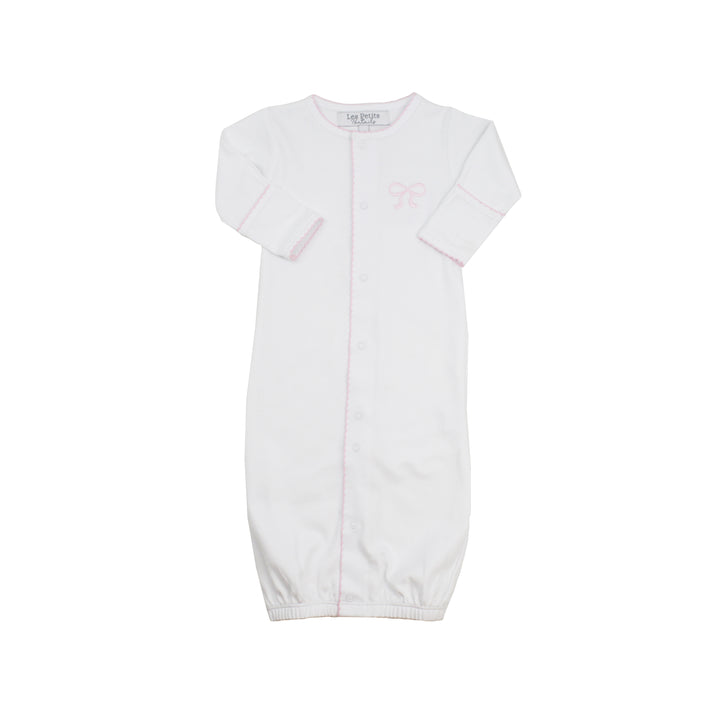 A white long-sleeve baby sleep sack with a button front, featuring a small light pink bow graphic on the left chest and a pink piping detail along the center seam.