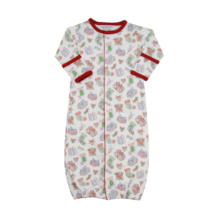 A baby sleep sack with a festive Christmas print, featuring a white background with illustrations of wrapped presents, Christmas trees, and Santa Claus. It has red trim along the collar, cuffs, and center front zipper.