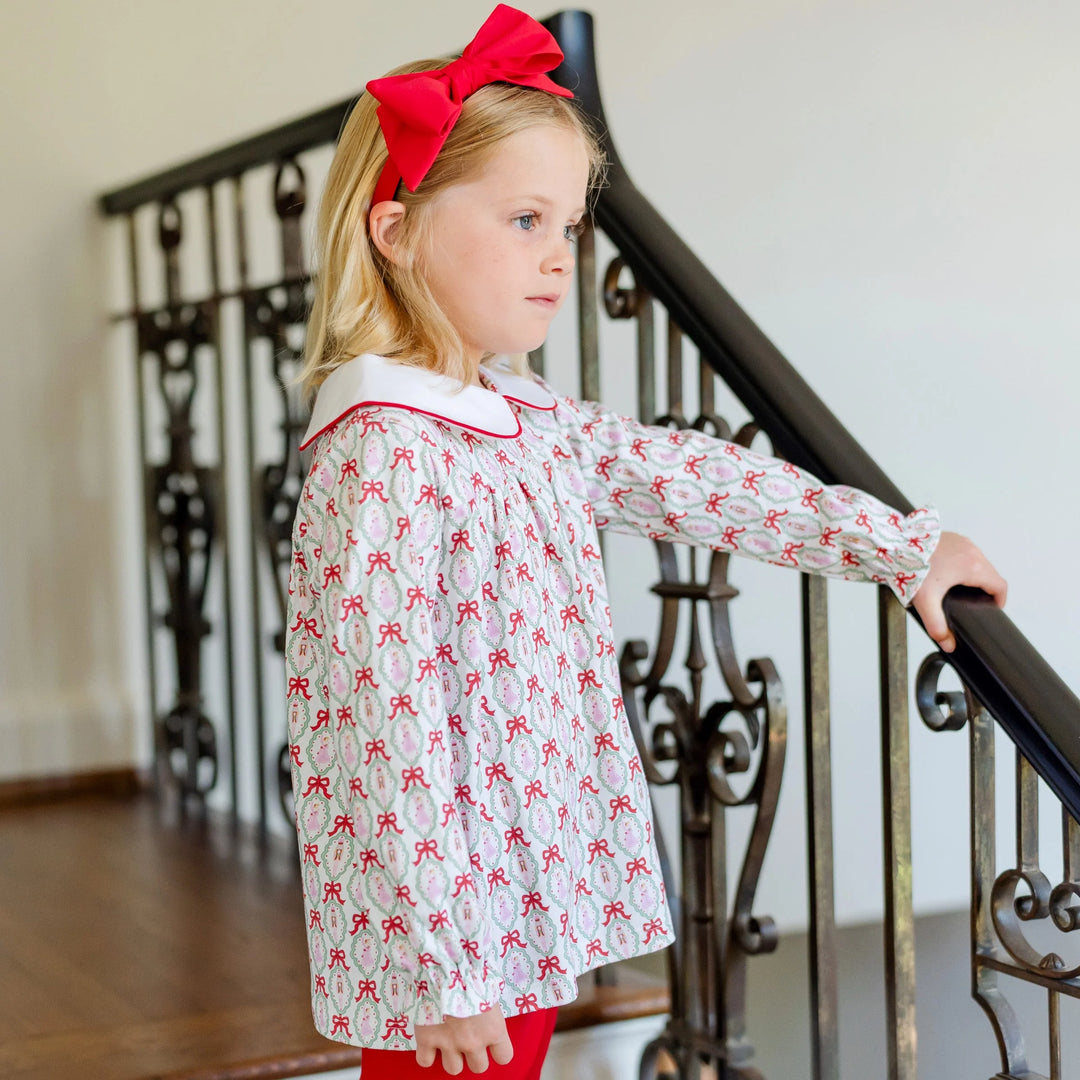 Young girl in a patterned dress with red bows standing on a staircase.