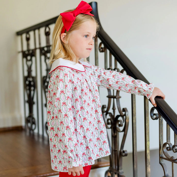 Young girl in a patterned dress with red bows standing on a staircase.