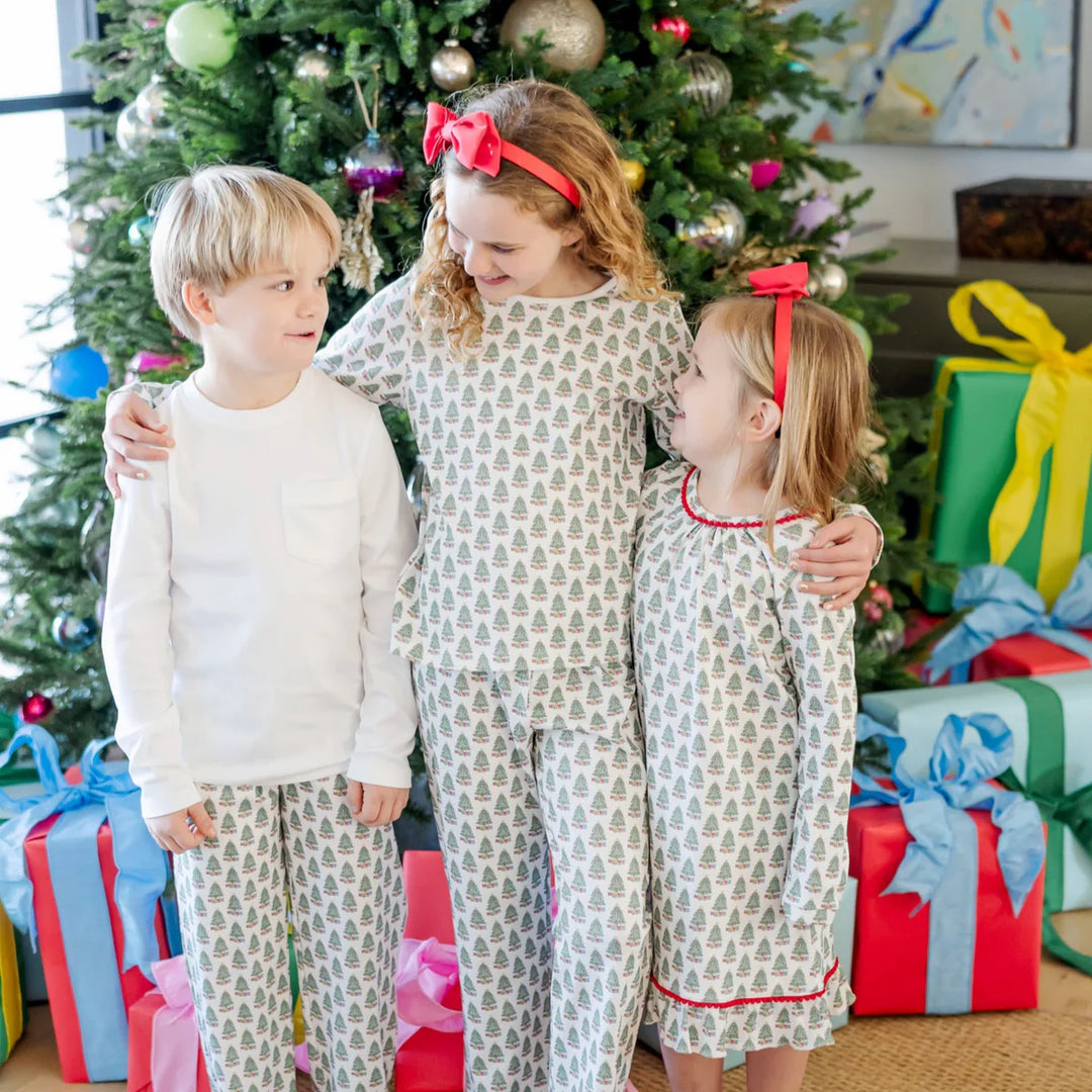Three children in matching pajamas standing in front of a Christmas tree with presents.