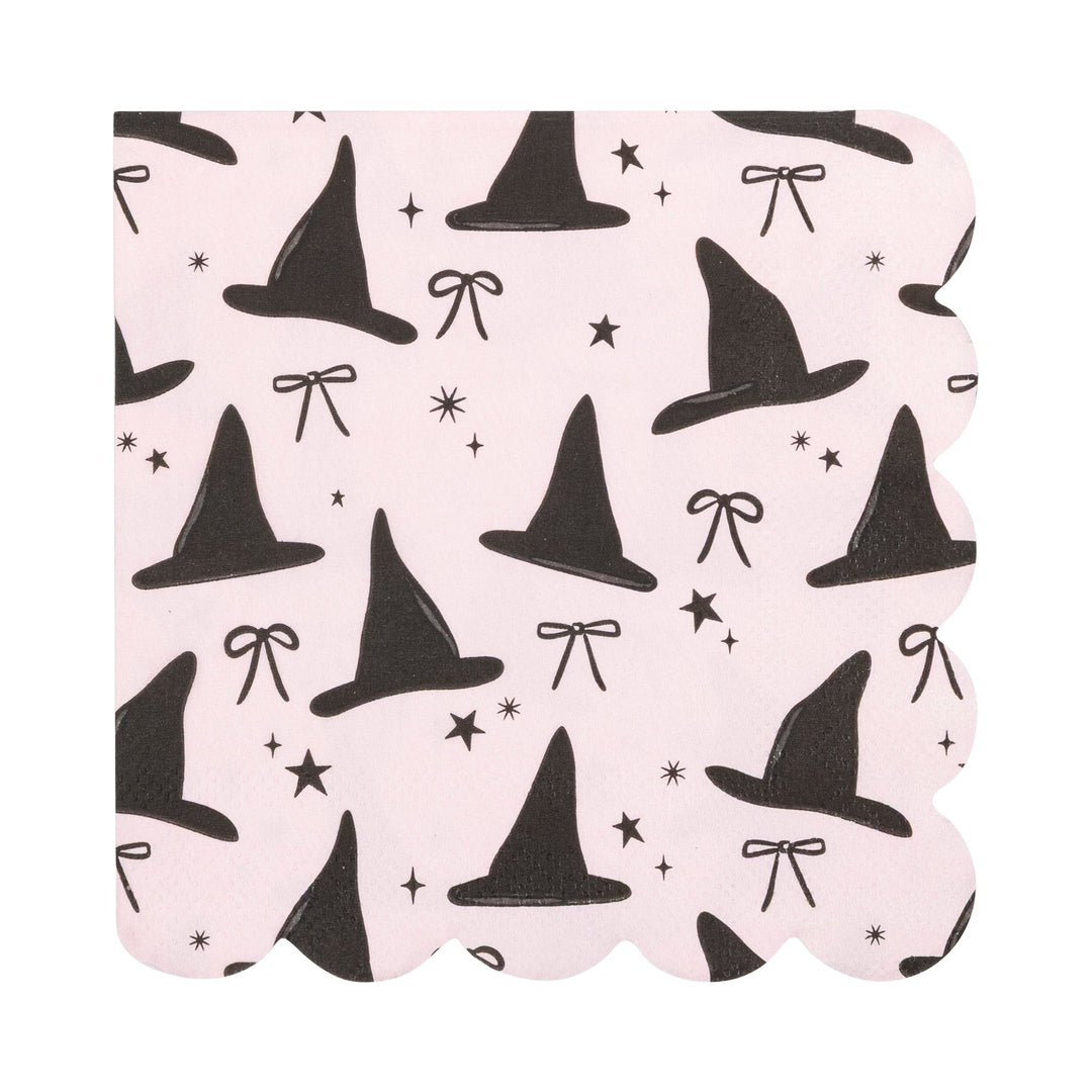A square paper napkin with scalloped edges, featuring a repeating pattern of black witch hats, bows, stars, and sparkles on a light pink background.