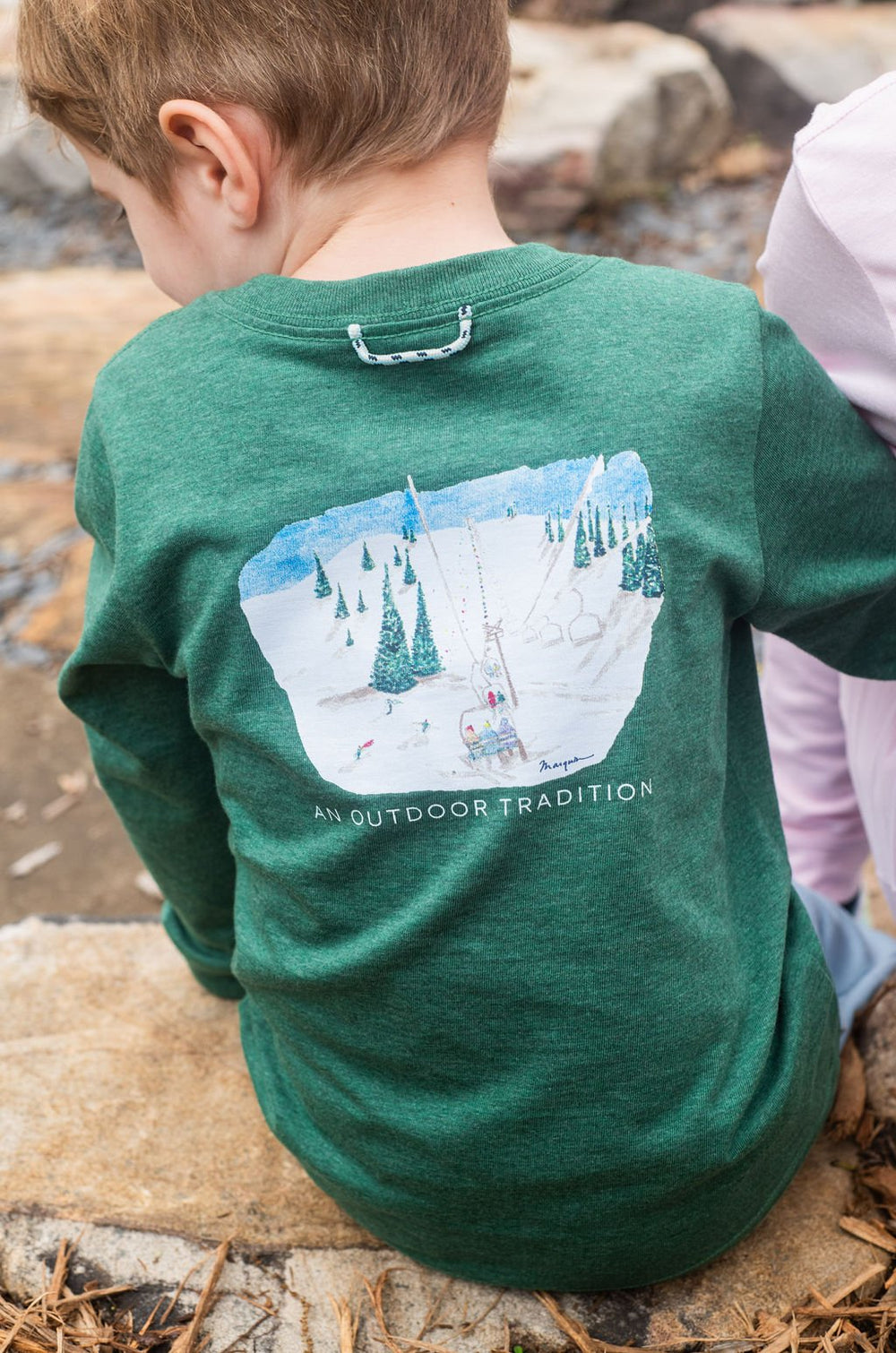 Child wearing a green shirt with a mountain graphic outdoors