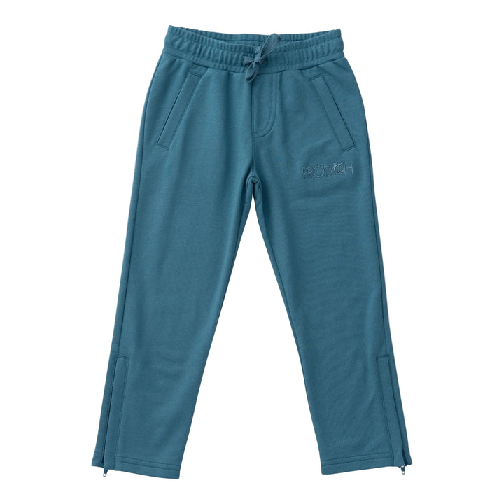 A pair of teal blue sweatpants with an elastic drawstring waist, side pockets, and a subtle embroidered logo on the left thigh, shown against a light beige background.