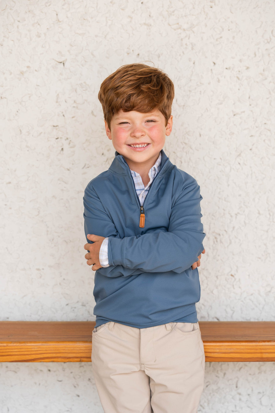 Young boy wearing a blue pullover with a white wall background