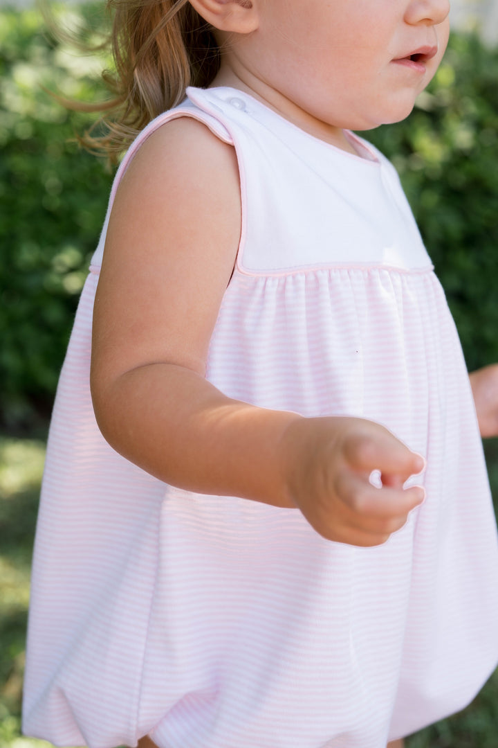 Child wearing a white sleeveless dress outdoors with greenery in the background