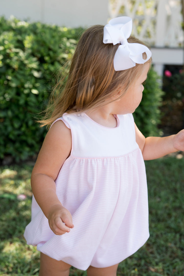 Young girl in a white dress with a large bow headband outdoors.