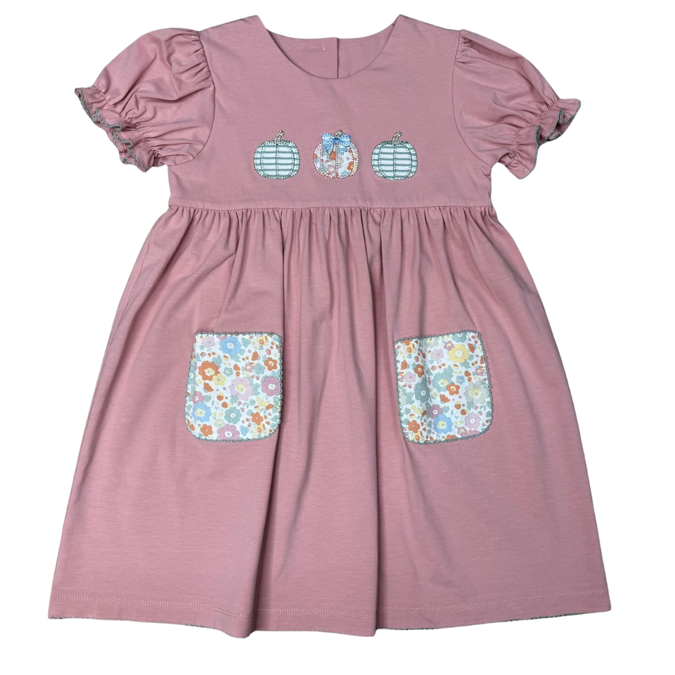 A dusty pink toddler dress with short puff sleeves, a gathered waist, three embroidered decorative motifs on the chest, and two floral patterned patch pockets on the front.